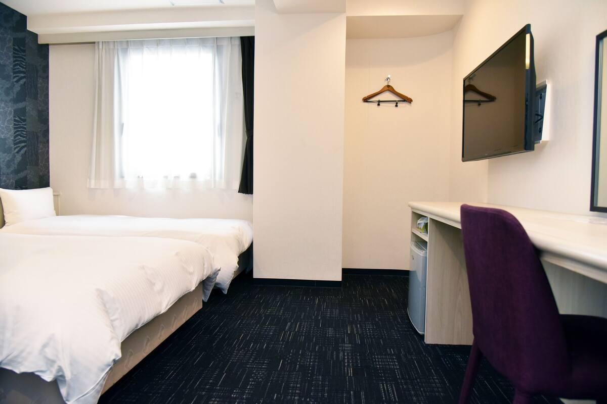 A hotel room with two beds, a desk, a chair, a mirror, and a window with curtains.