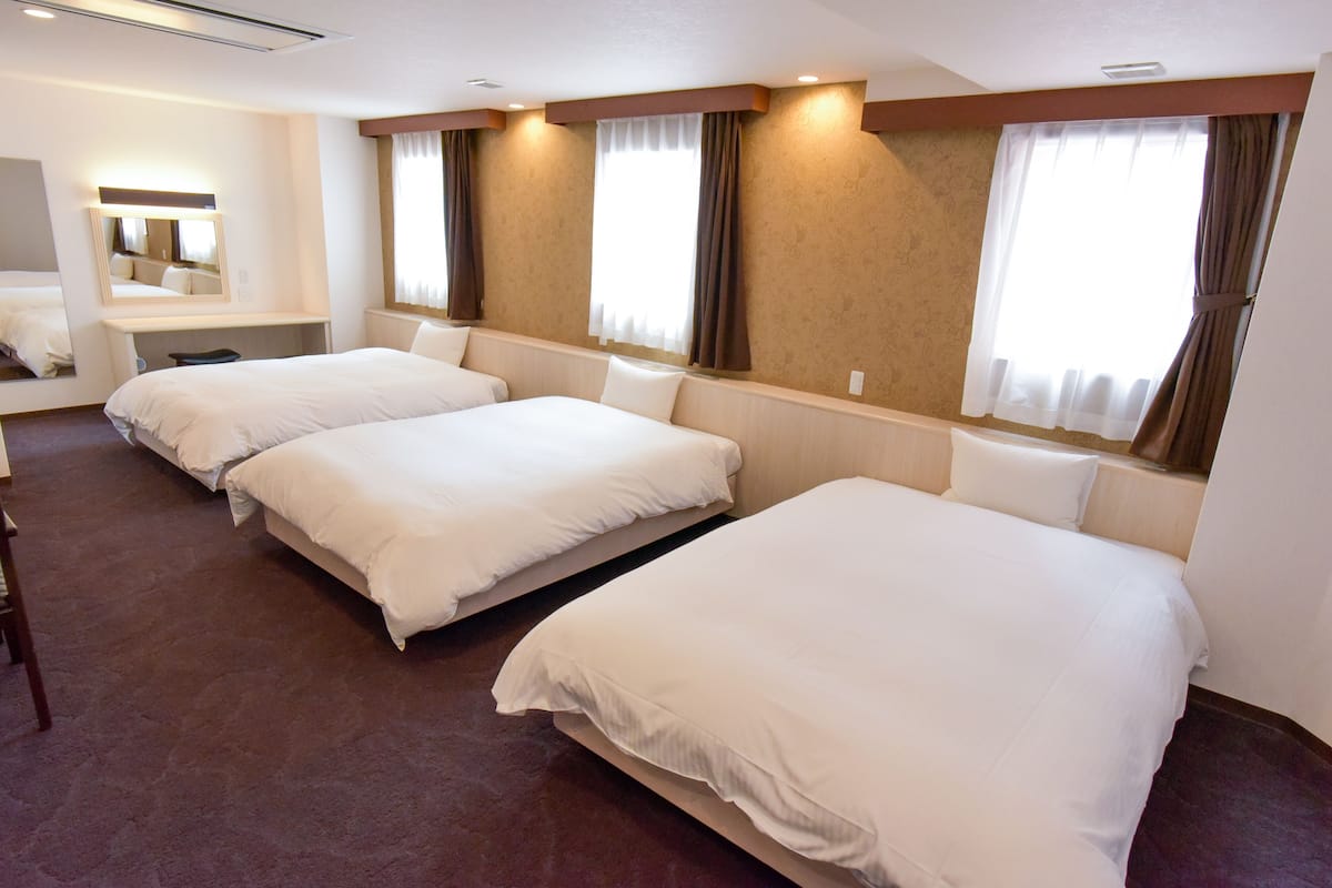 A hotel room with two single beds, a desk, and a mirror.
