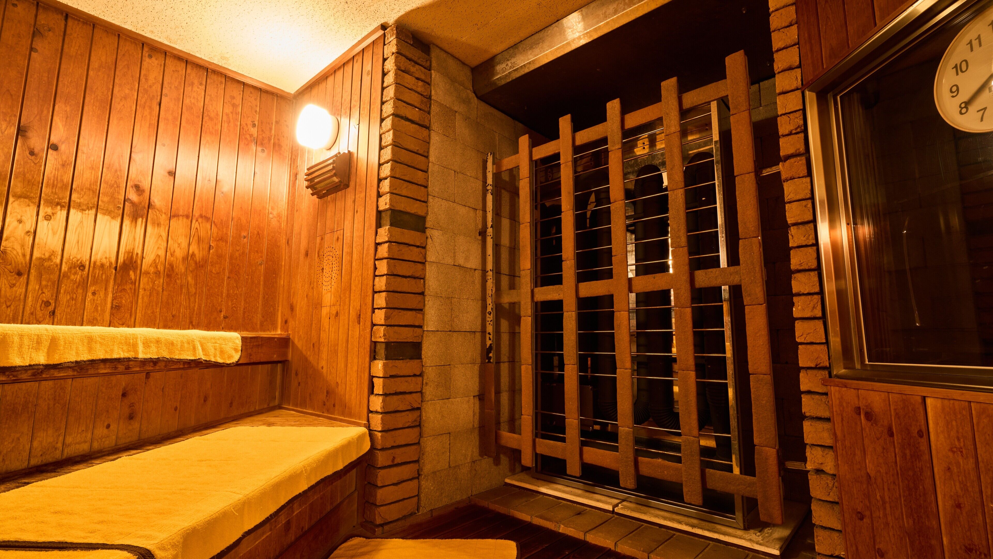A wooden interior with a bench, a window with metal bars, and a clock on the wall.