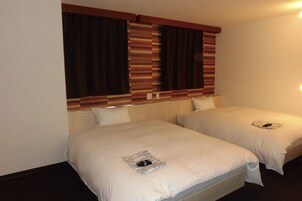 Una habitación de hotel con dos camas individuales, un cabecero a rayas y un ventanal con cortinas.