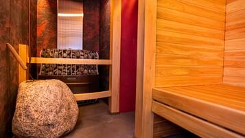 A sauna room with wooden benches, a stone bench, and a wall with a red panel.