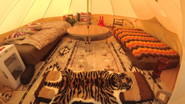 Interior de una tienda de campaña con una mesa redonda, un sofá, un felpudo de tigre y un calentador.