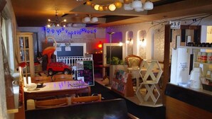 Interior de restaurante con un letrero de neón, un coche de juguete rojo, una silla de madera, una mesa y un armario blanco.