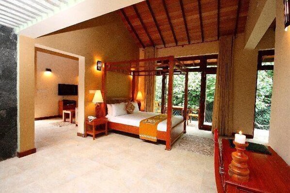 A bedroom with a four-poster bed, bedside lamps, a TV, and a window with a view of greenery.