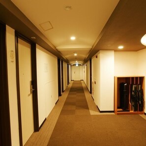 A hotel corridor with doors on both sides, a carpeted floor, and a wooden shoe rack on the right. - Century Art (Fukuoka)