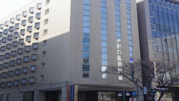 En bygning i flere etager med moderne arkitektur, der har en markant indgang med en glasfacade og et skilt, der angiver, at det er et hotel.