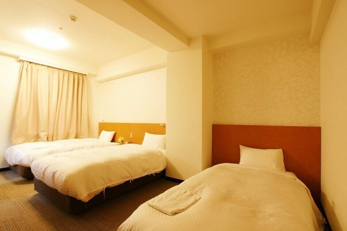 A hotel room with two beds, a headboard, and a window with curtains.