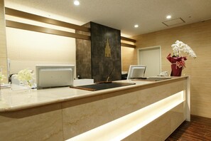 A reception desk with a marble top, a dark accent wall, and a vase of white orchids. - Century Art (Fukuoka)