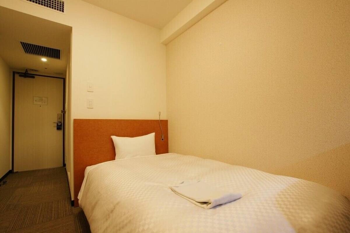 A hotel room with a single bed, a wooden headboard, a door, and a carpeted floor.
