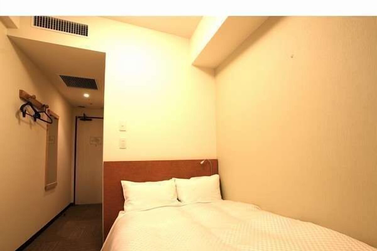 A hotel room with a bed, a wooden headboard, and a door leading to another room.