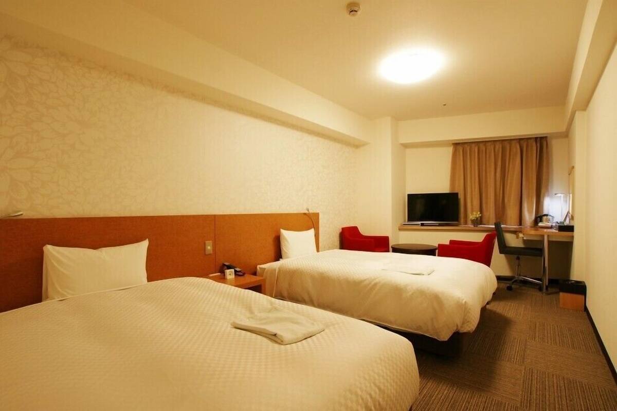 A hotel room with two beds, a desk with a chair, a television, and a window with curtains.