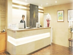 A reception desk with a person standing behind it, a computer, and a vase with flowers. - Century Art (Fukuoka)