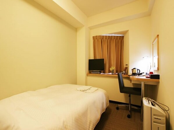 A hotel room with a bed, a desk with a computer, a chair, and a window with curtains.