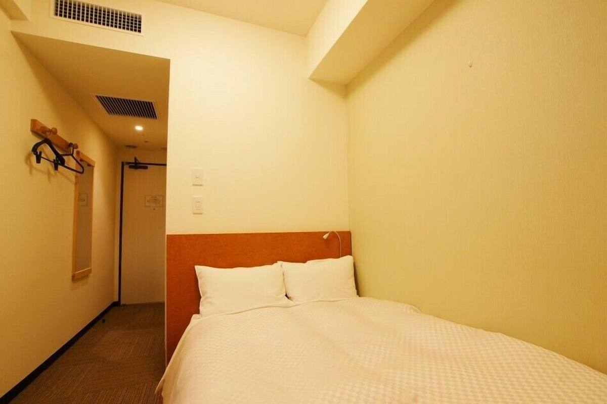 A hotel room with a bed, a wooden headboard, a coat rack, and a door leading to another room.