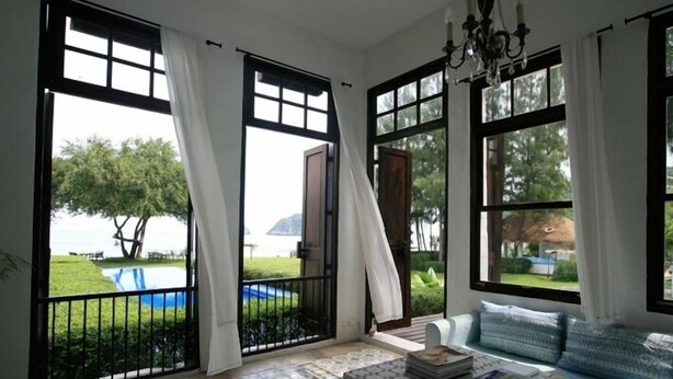Una habitación con ventanas amplias, un candelabro y vistas a una piscina y follaje.