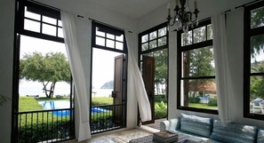 Una habitación con ventanas amplias, un candelabro y vistas a una piscina y follaje.