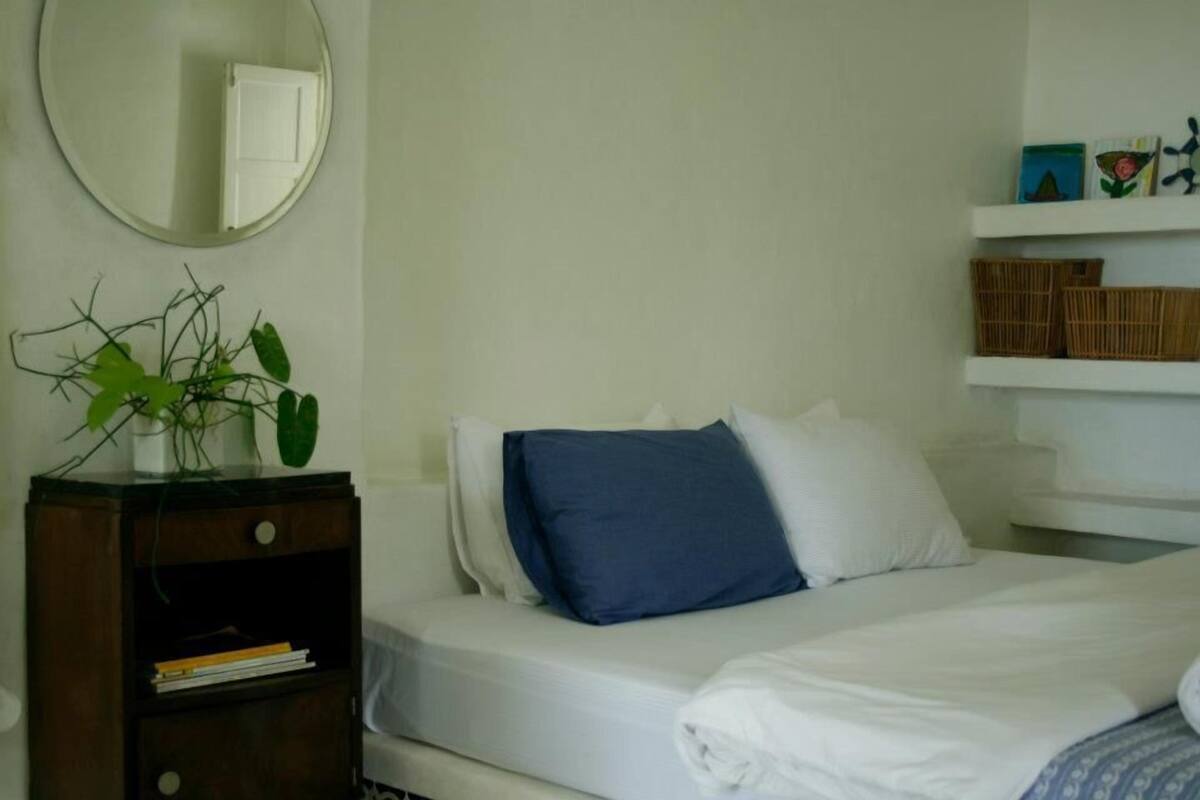 Quarto de hotel com cama, mesa de cabeceira, espelho e prateleira com objetos decorativos.