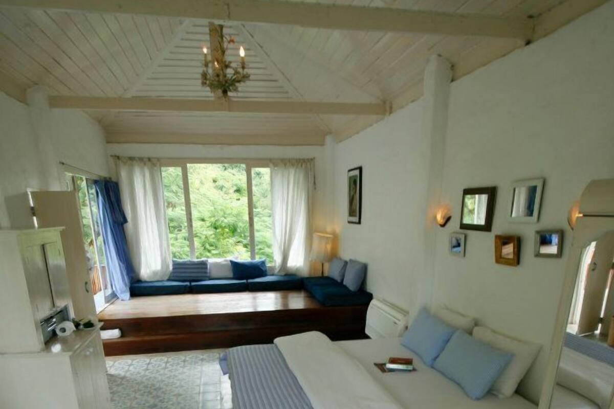 Quarto com cama, um banco, janela com cortinas, lustre e piso estampado.