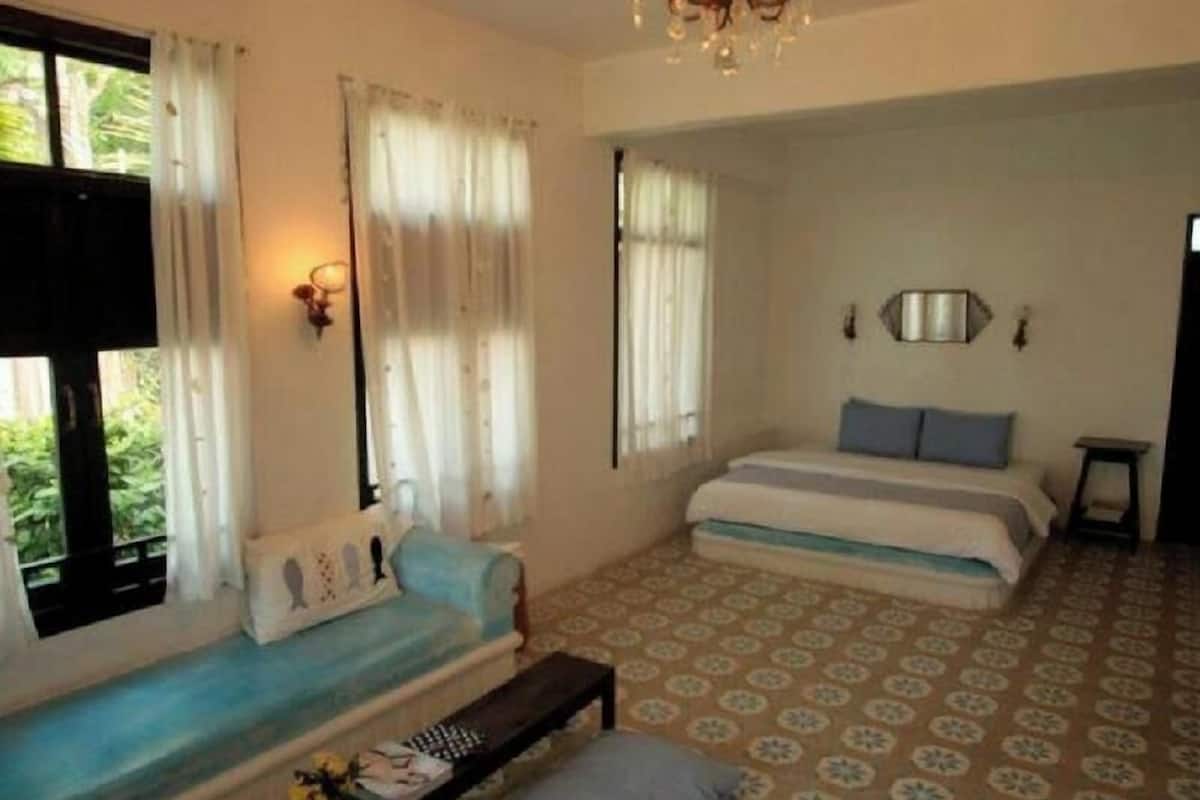Quarto com cama, sofá, uma mesinha, um candelabro e piso estampado.