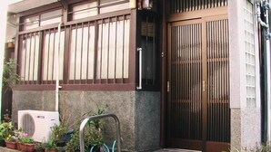 A building with a gated entrance, a small air conditioning unit, and potted plants. - Kyo no Machiya Uenoya (Kyoto)