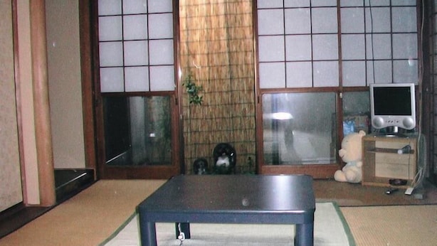 A traditional Japanese room with tatami flooring, a sliding door, a television on a stand, and a small table. - Kyo no Machiya Uenoya (Kyoto)