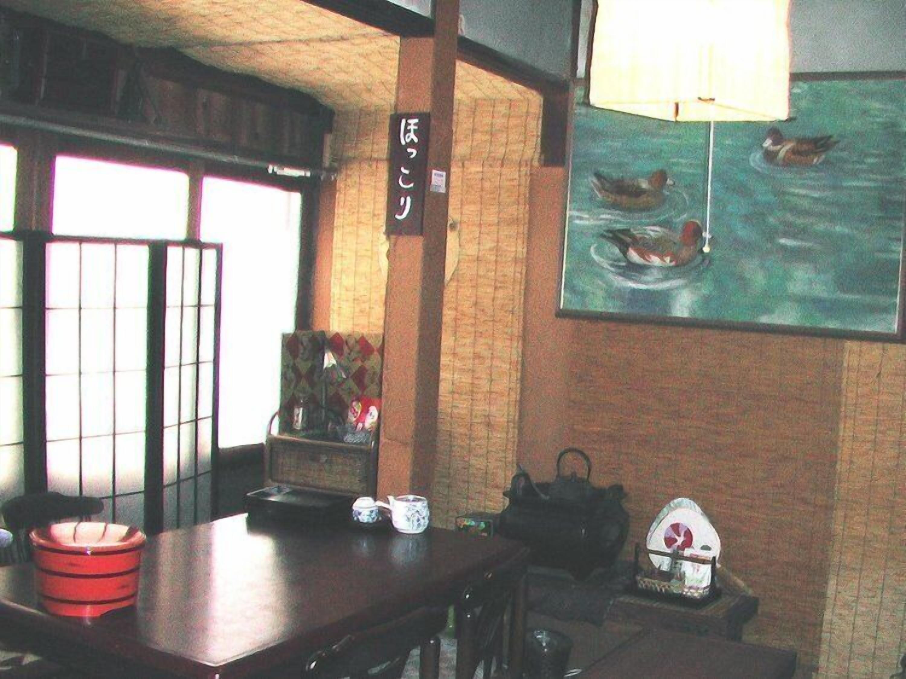 A traditional Japanese room with tatami flooring, a low table with a tea set, a hanging lamp, and a painting of ducks on water.