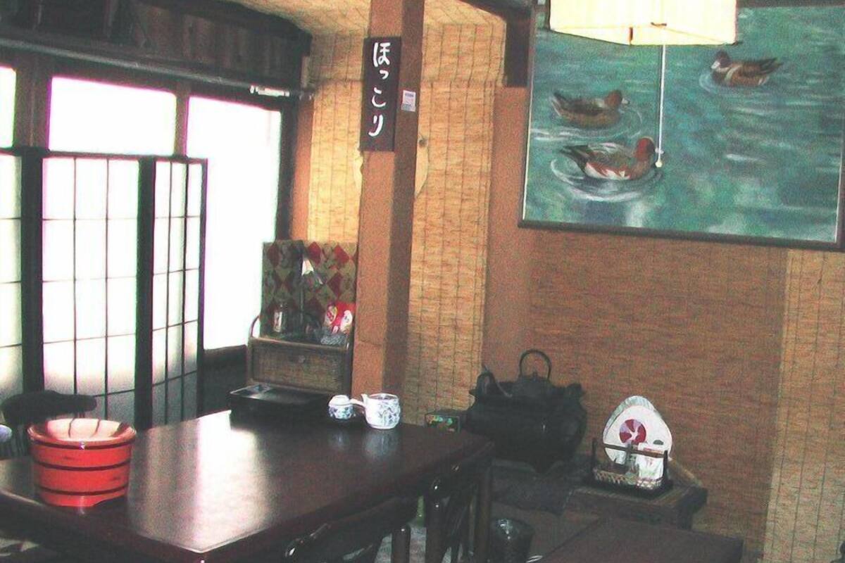 Ein traditioneller japanischer Raum mit Tatami-Boden, einem niedrigen Tisch mit Tee-Set, einer Hängeleuchte und einem Gemälde von Enten auf dem Wasser.
