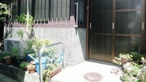 A traditional Japanese building with a sliding door, a small garden area with potted plants, and a concrete step leading to the entrance. - Kyo no Machiya Uenoya (Kyoto)
