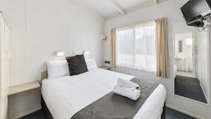 Een hotelkamer met een bed, een nachtkastje, een aan de muur bevestigde televisie en een raam met gordijnen.