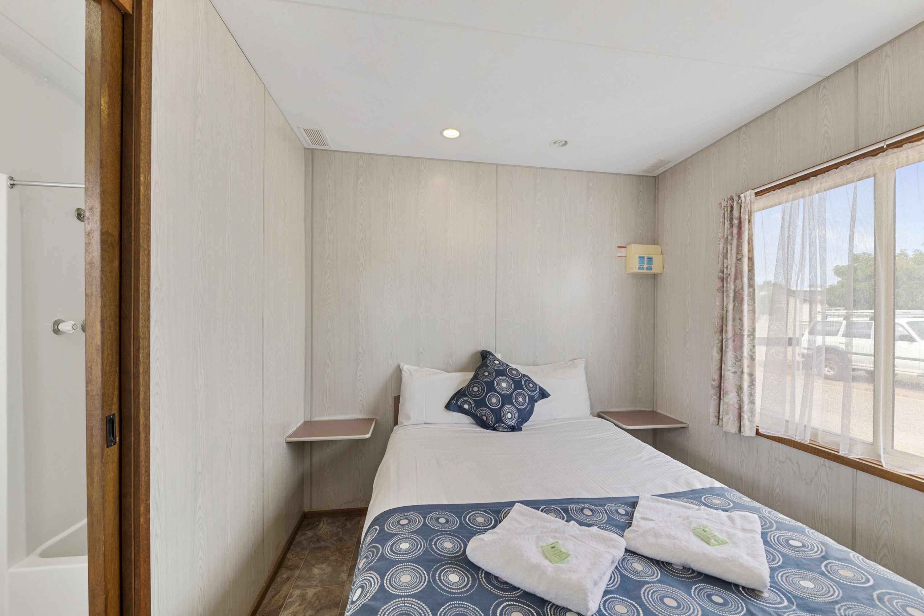 A hotel room with a bed, two bedside tables, a window with curtains, and a view of the outside.