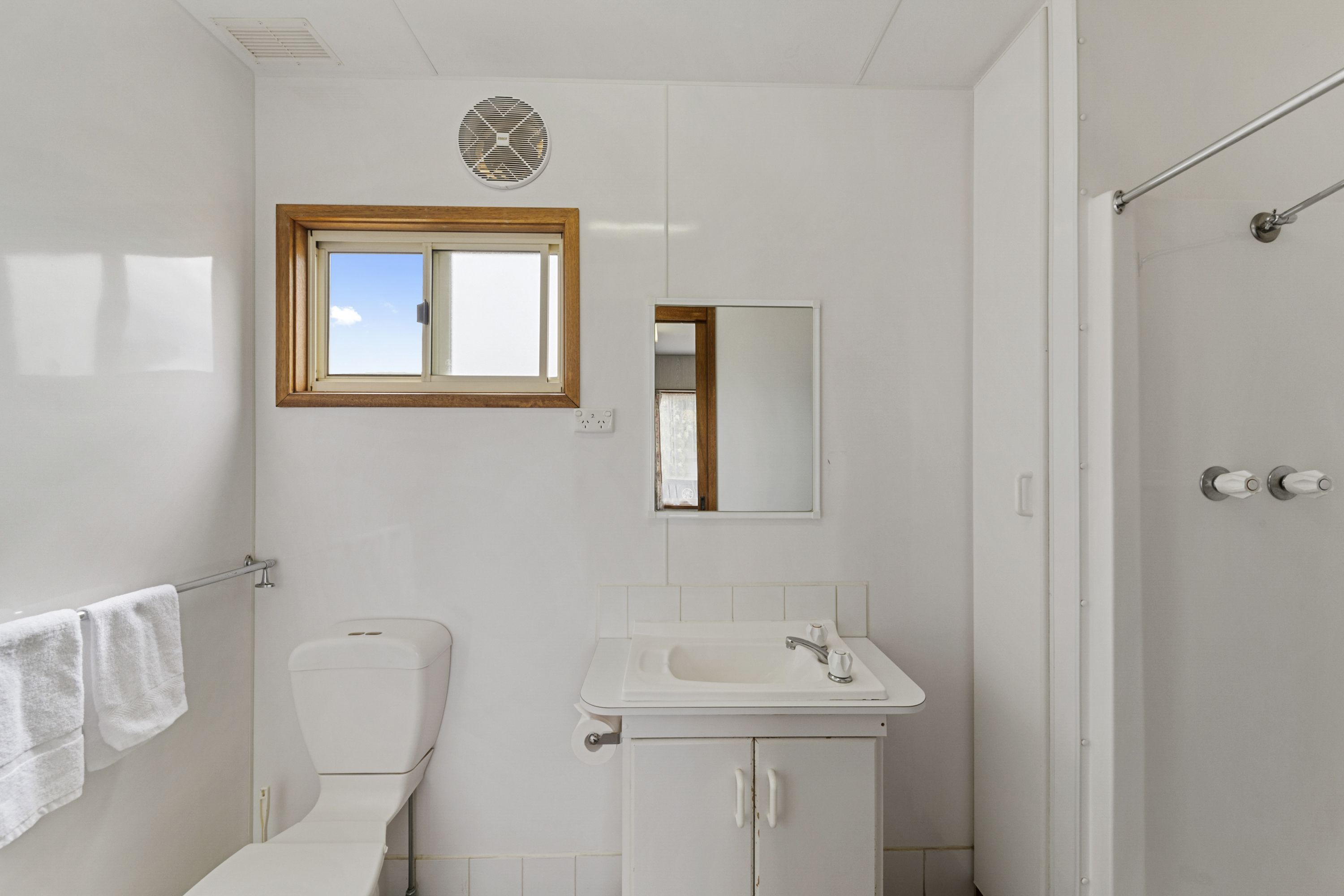 A small, white bathroom with a toilet, sink, and a window above the sink.