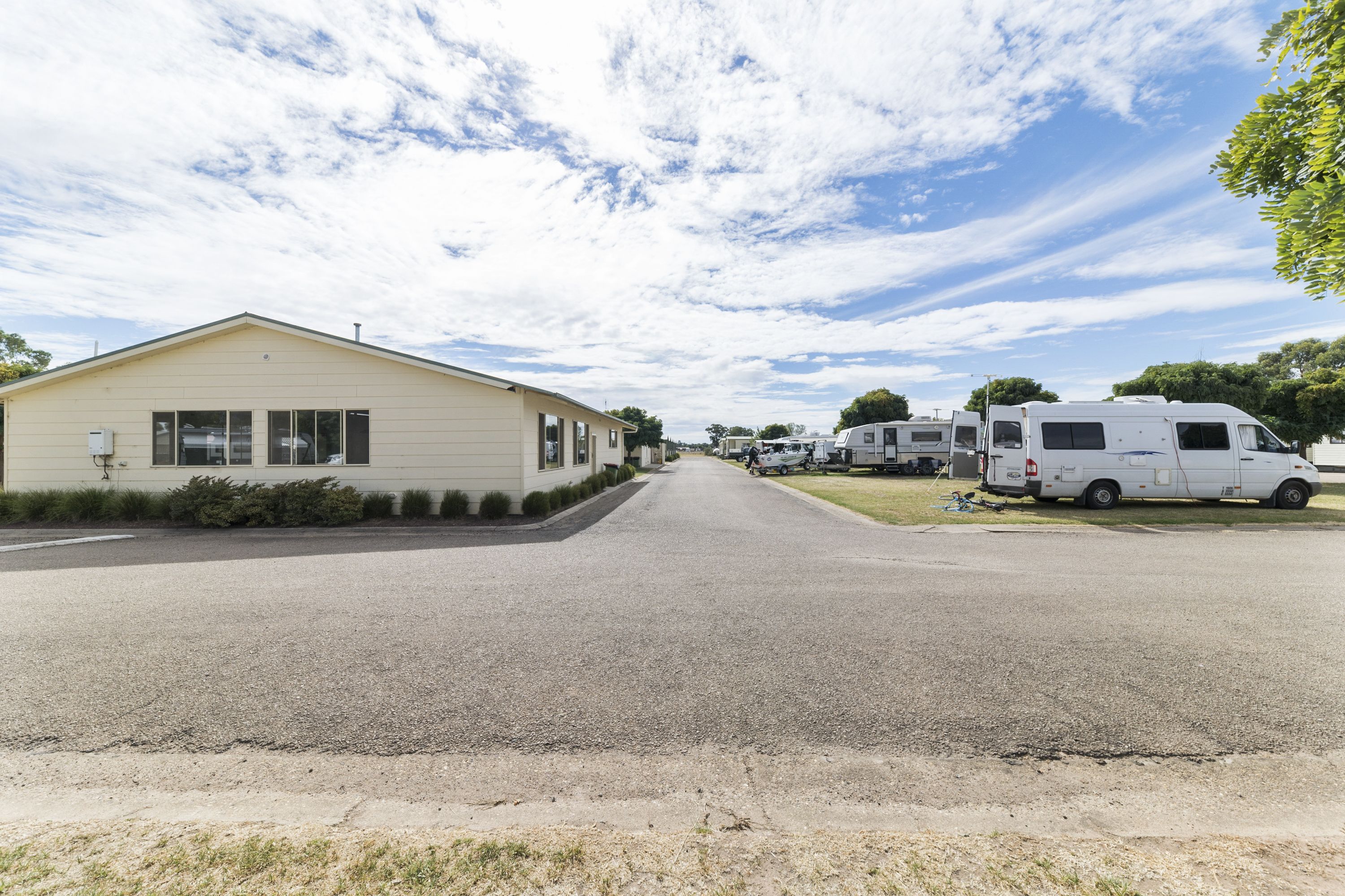 A street with a single-story house and several RVs parked on the side.