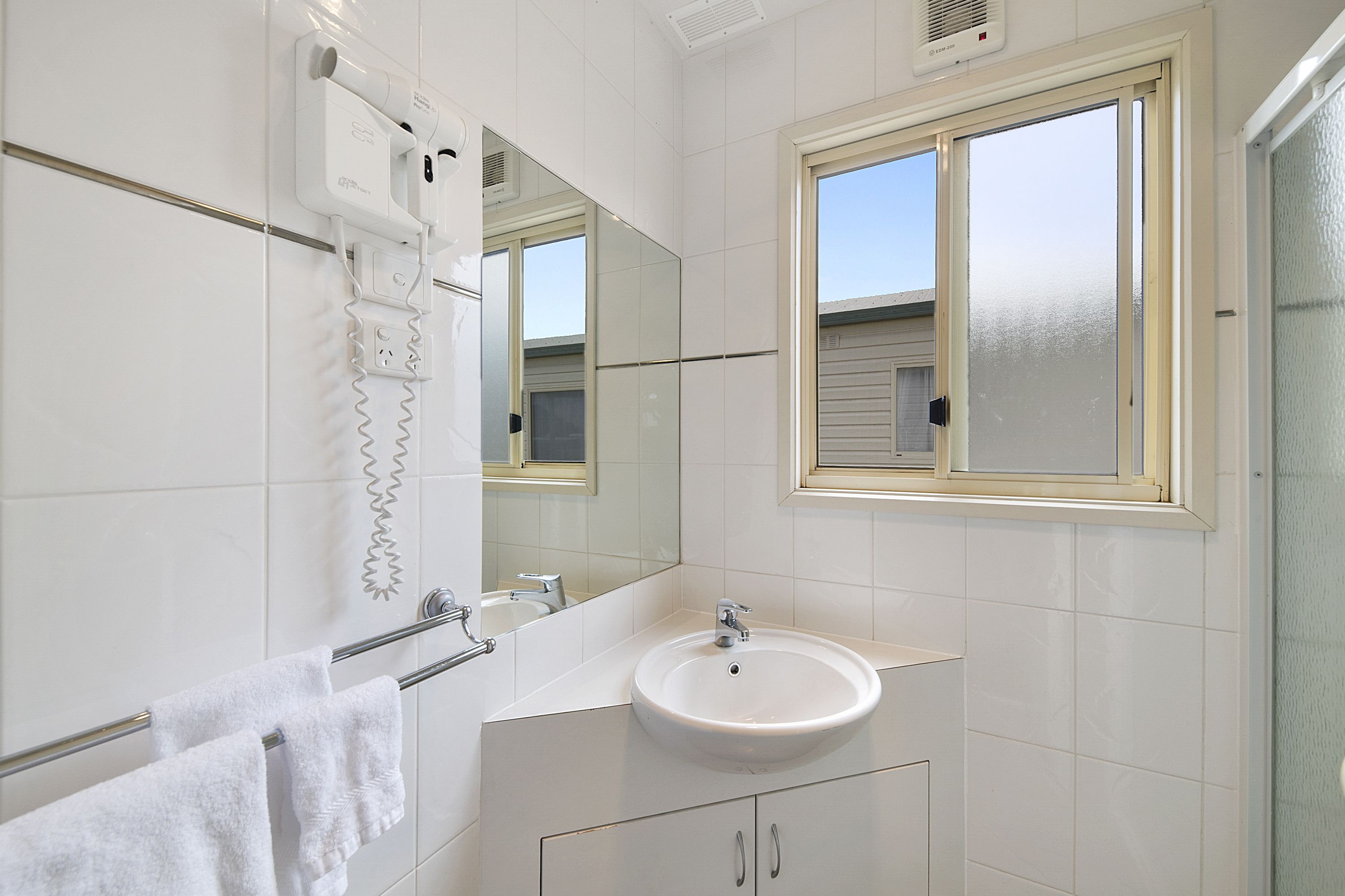 A bathroom with a white sink, a towel rack, a mirror, and a window.