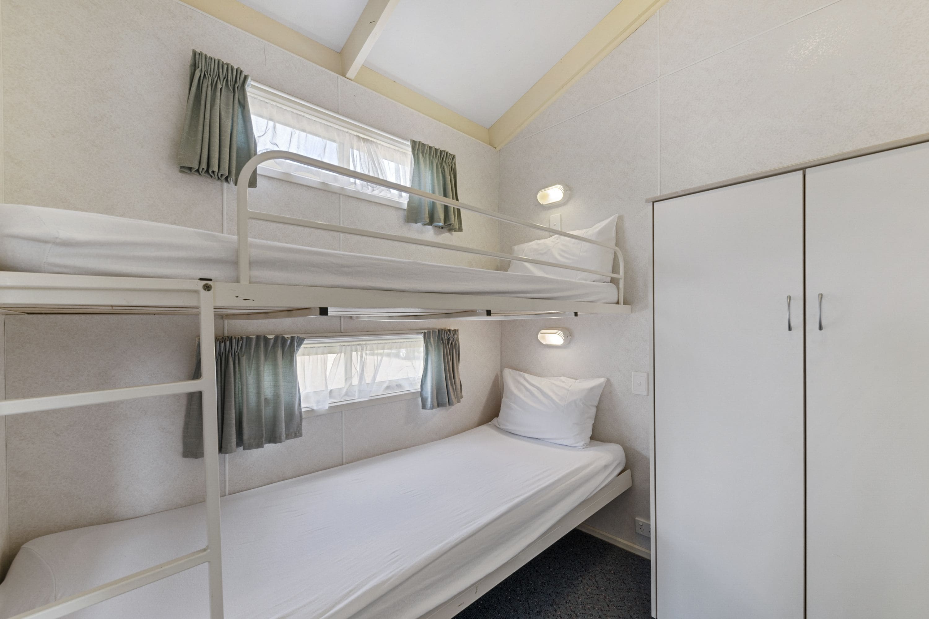 Een slaapkamer met een stapelbed, een kledingkast en een raam met gordijnen.