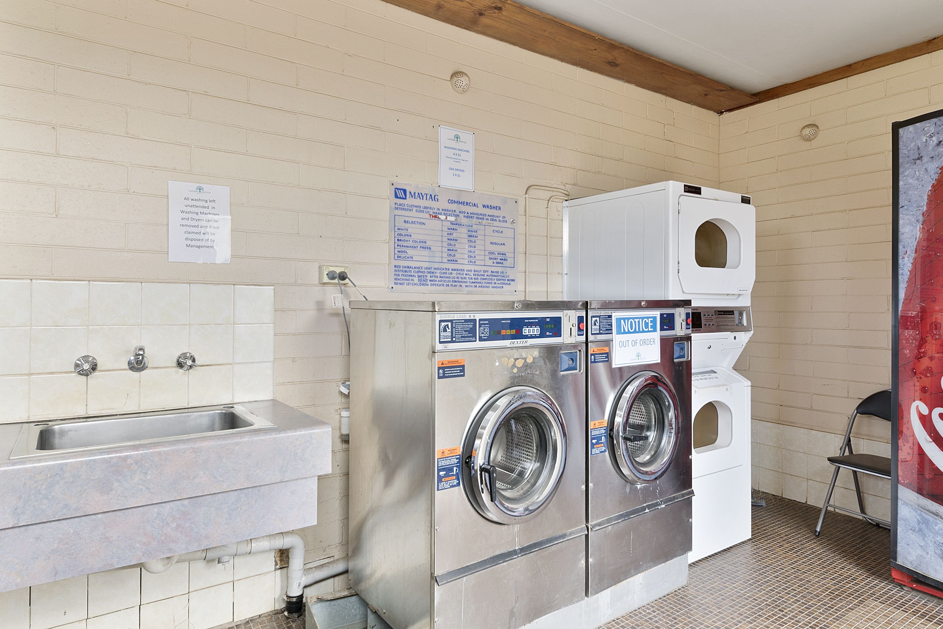 A laundry facility with two washing machines, a sink, and a notice board.