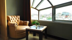 A room with a large window, a tufted leather armchair, and a small table with a plant.