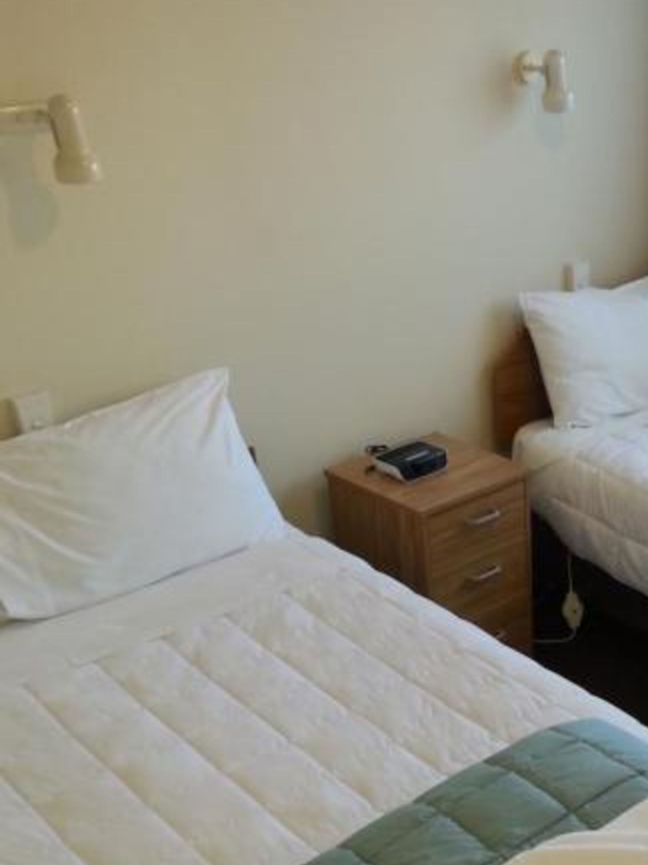 A single bed with a quilted headboard, a bedside table with a lamp, and a wall-mounted light fixture.