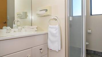 Une salle de bain avec un meuble-lavabo blanc, un porte-serviettes, un miroir, des toilettes et un espace douche.