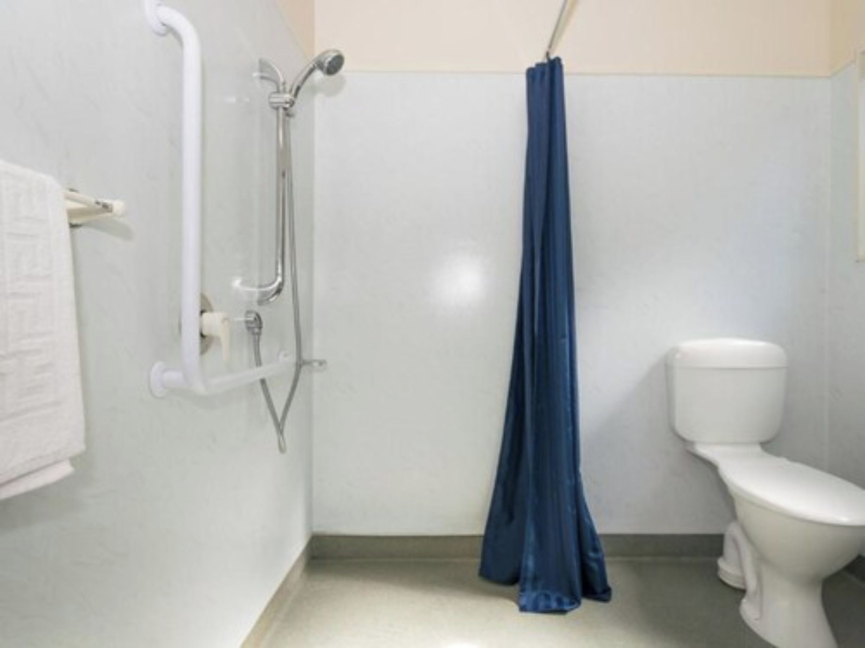 A bathroom with a white toilet, a shower with a blue curtain, and a grab bar on the wall.