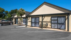 A motel with a parking lot, a covered outdoor seating area, and a palm tree. - Ashleigh Court Motel (Blenheim)