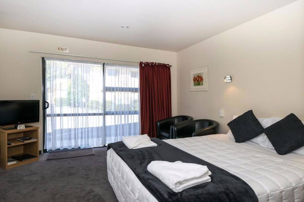 A hotel room with a bed, a TV, a desk, and a chair.