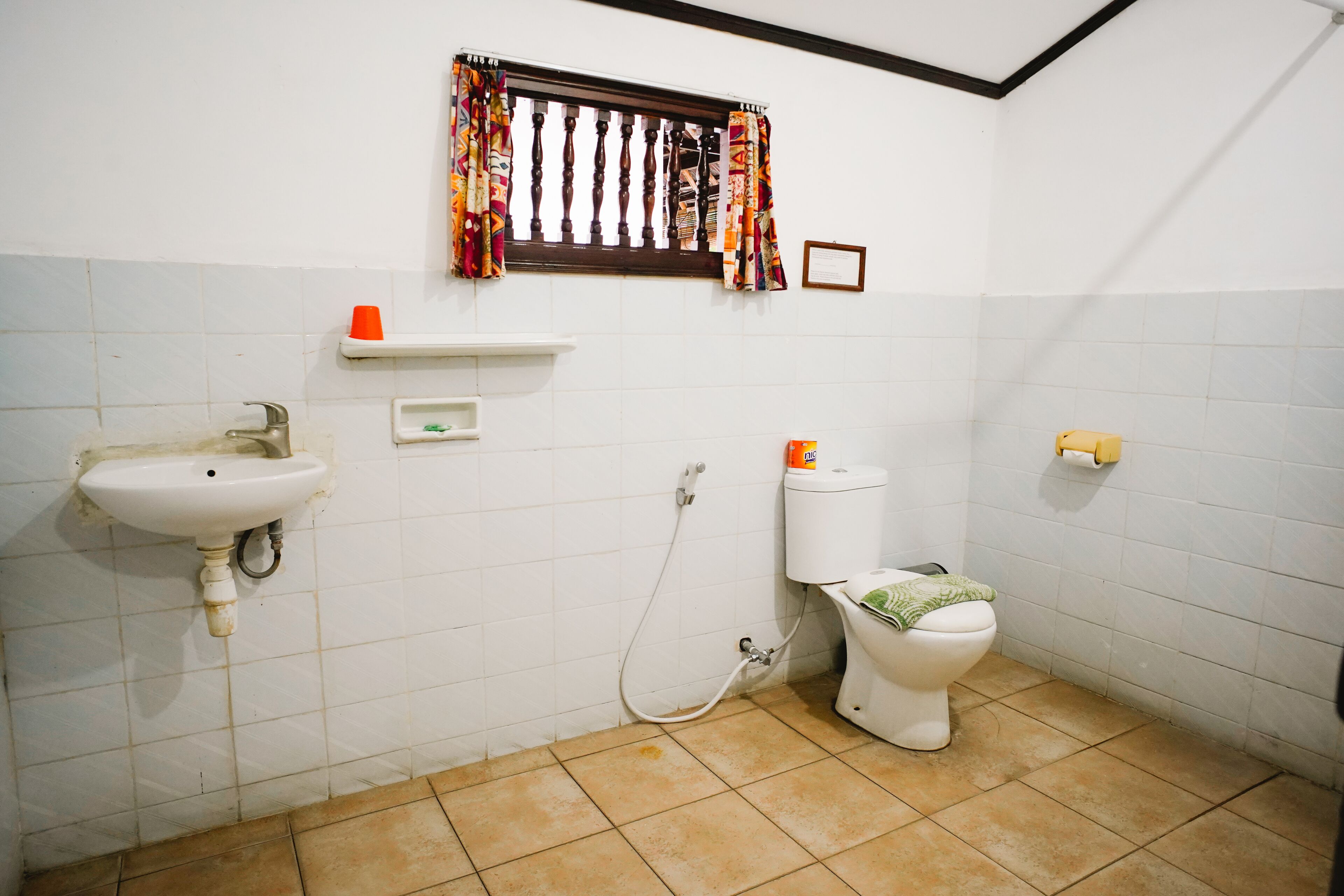A bathroom with a sink, toilet, and window with curtains.