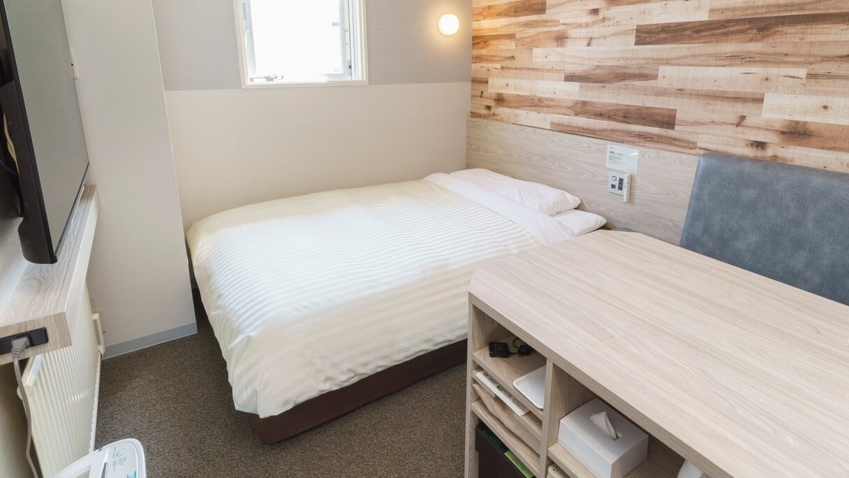 A compact room with a bed, a desk, a television, and a wooden wall.