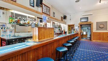 A bar area with stools, a counter with various bottles, and a dartboard on the wall.