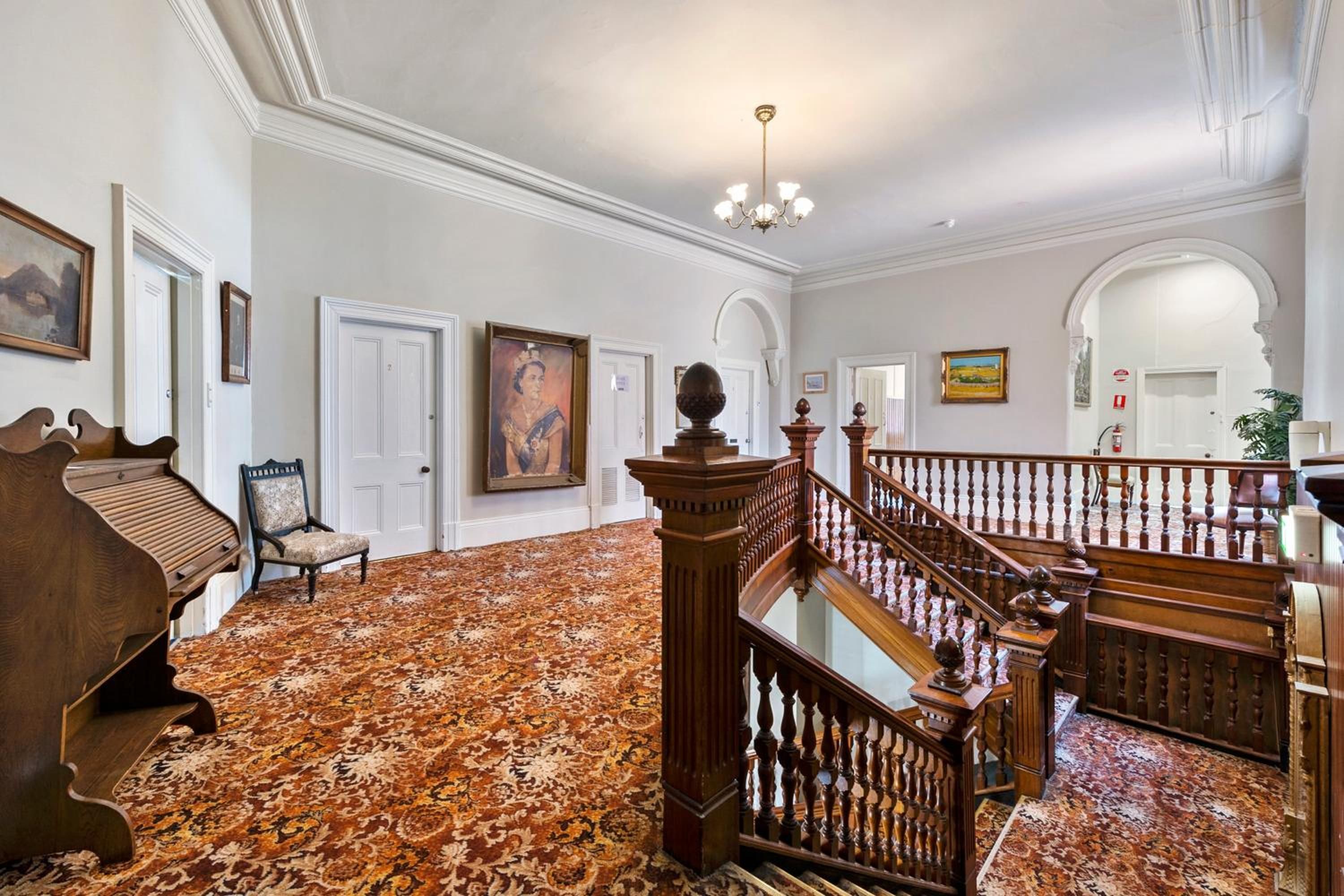 A grand hallway with a wooden staircase, a piano, and a large painting on the wall.
