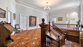 A grand hallway with a wooden staircase, a piano, and a large painting on the wall.