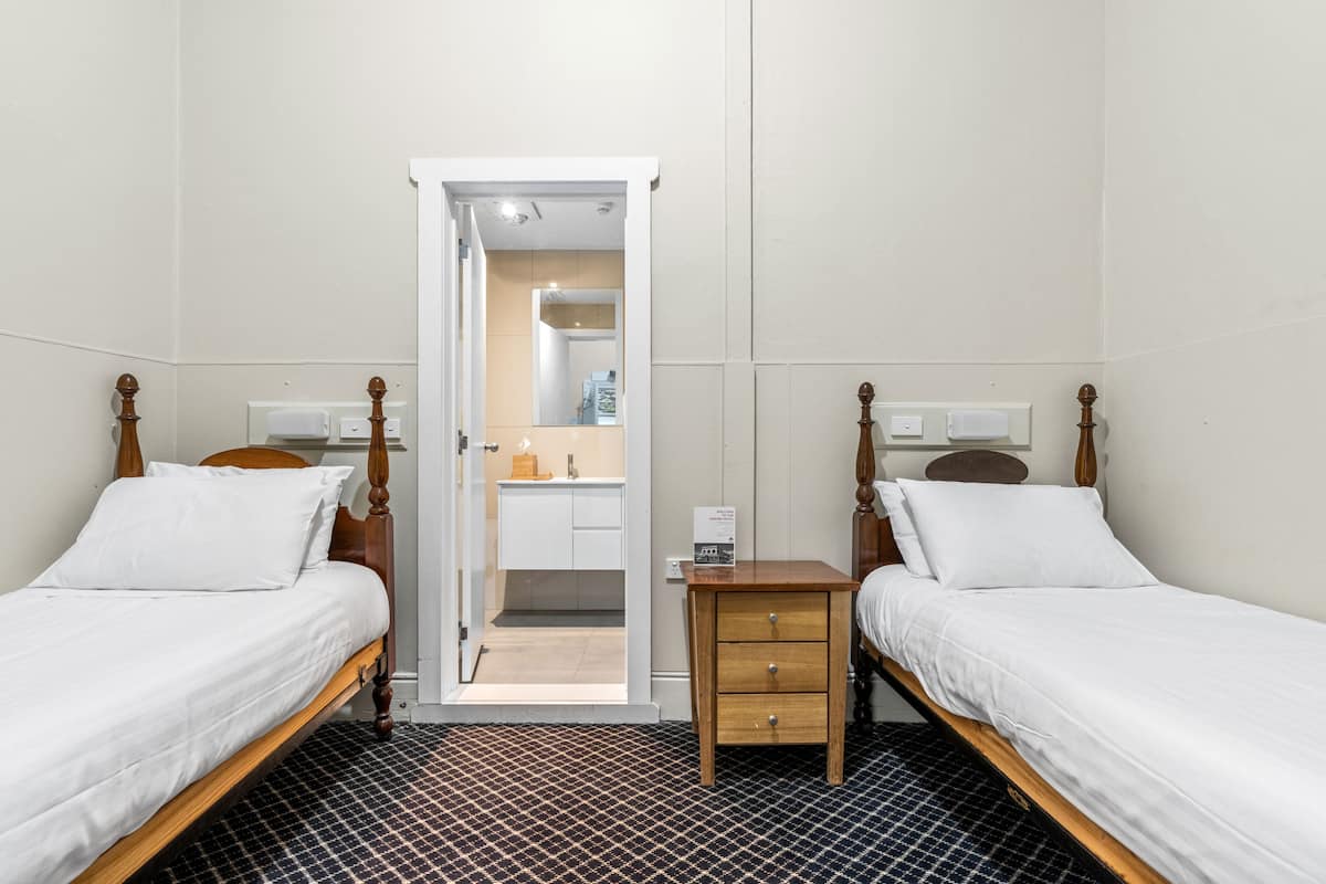 Ein Doppelzimmer mit zwei Einzelbetten, einem kleinen Nachttisch, einem weißen Badezimmer mit Spiegel und einem Fliesenboden.