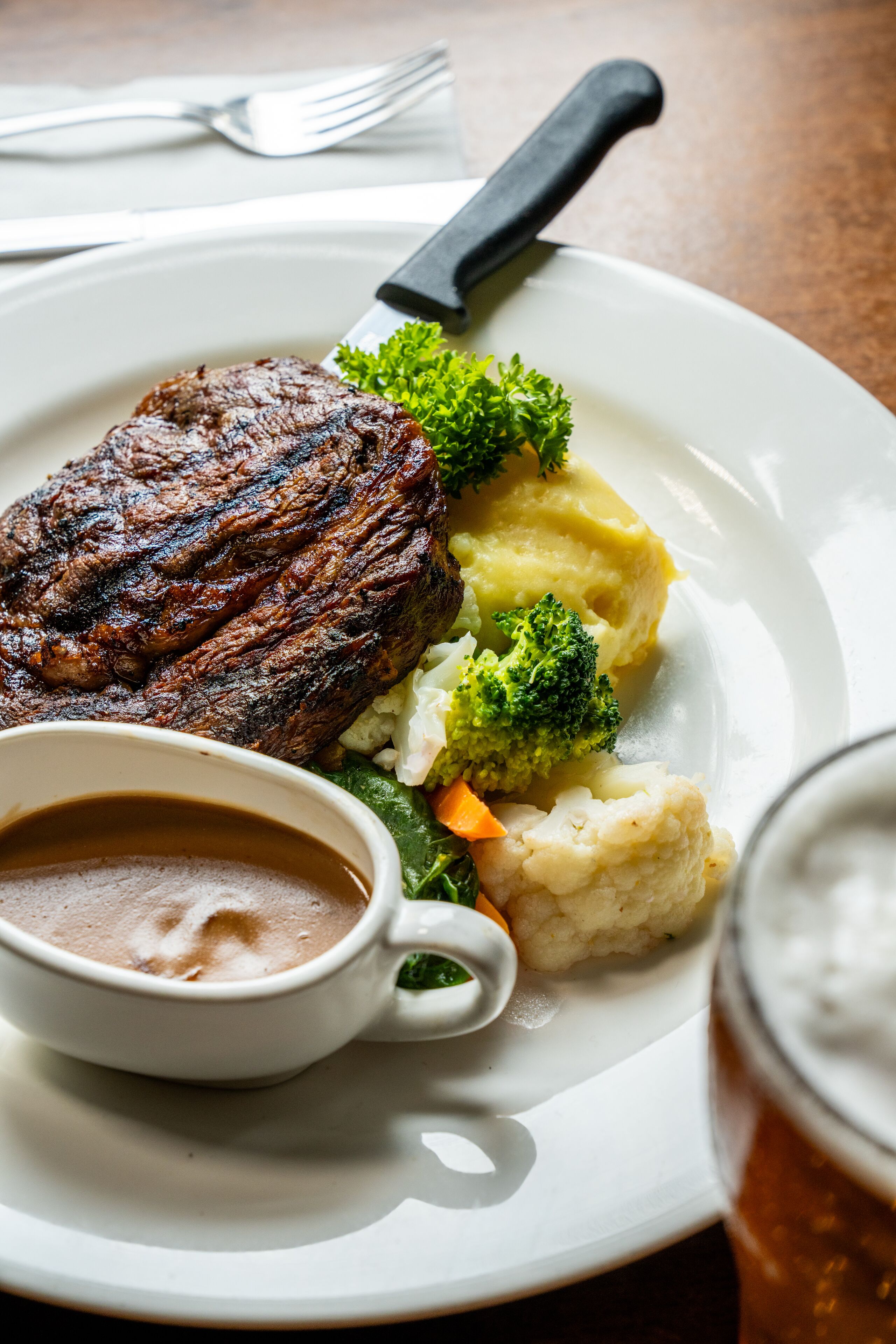 A plate with a steak, mashed potatoes, broccoli, and a gravy boat.
