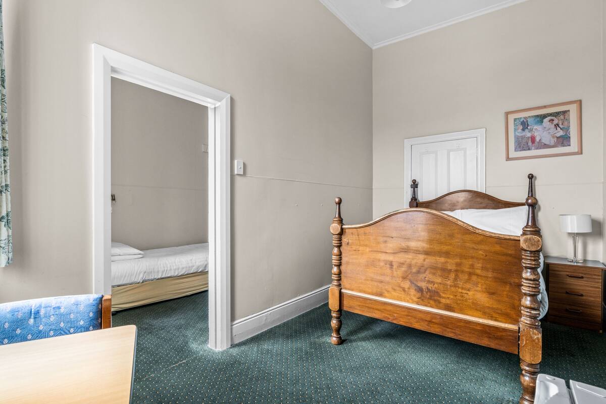 Ein Schlafzimmer mit einem hölzernen Bett, einem kleinen Nachttisch, einem Sessel und einer Tür zu einem anderen Raum.