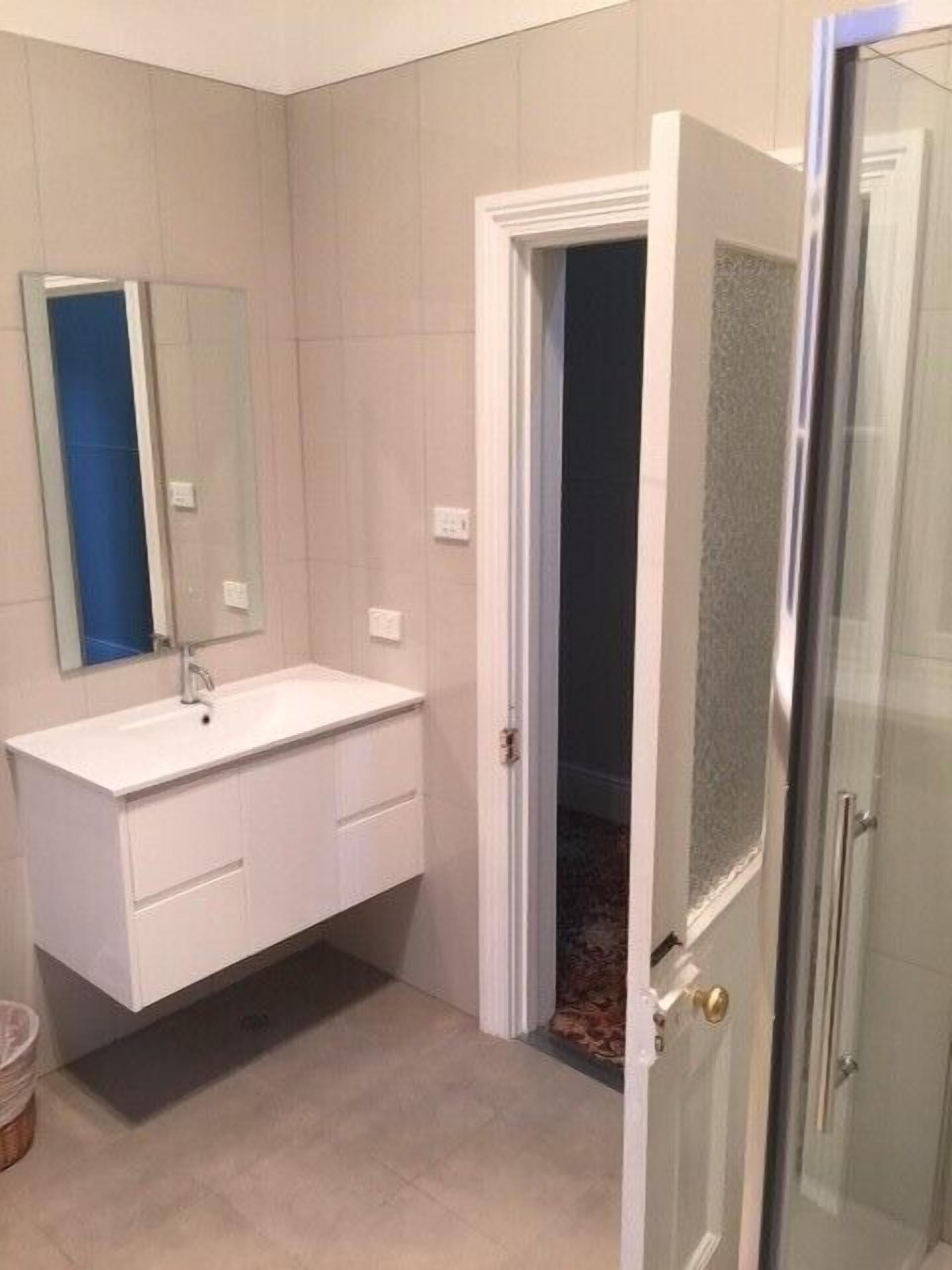 Ein Badezimmer mit weißem Waschtisch, einem Spiegel und einer Duschkabine aus Glas.